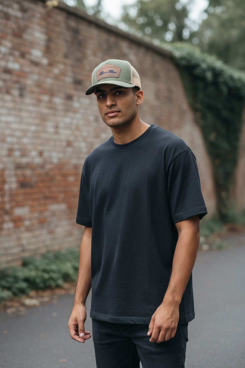 Man wearing a black t-shirt and green cap standing in front of a brick wall.